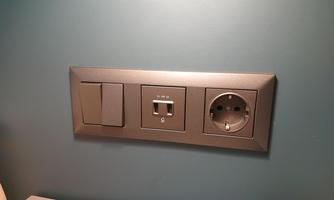 A modern wall socket with a switch and a LAN connection. The surface is in an elegant gray tone.