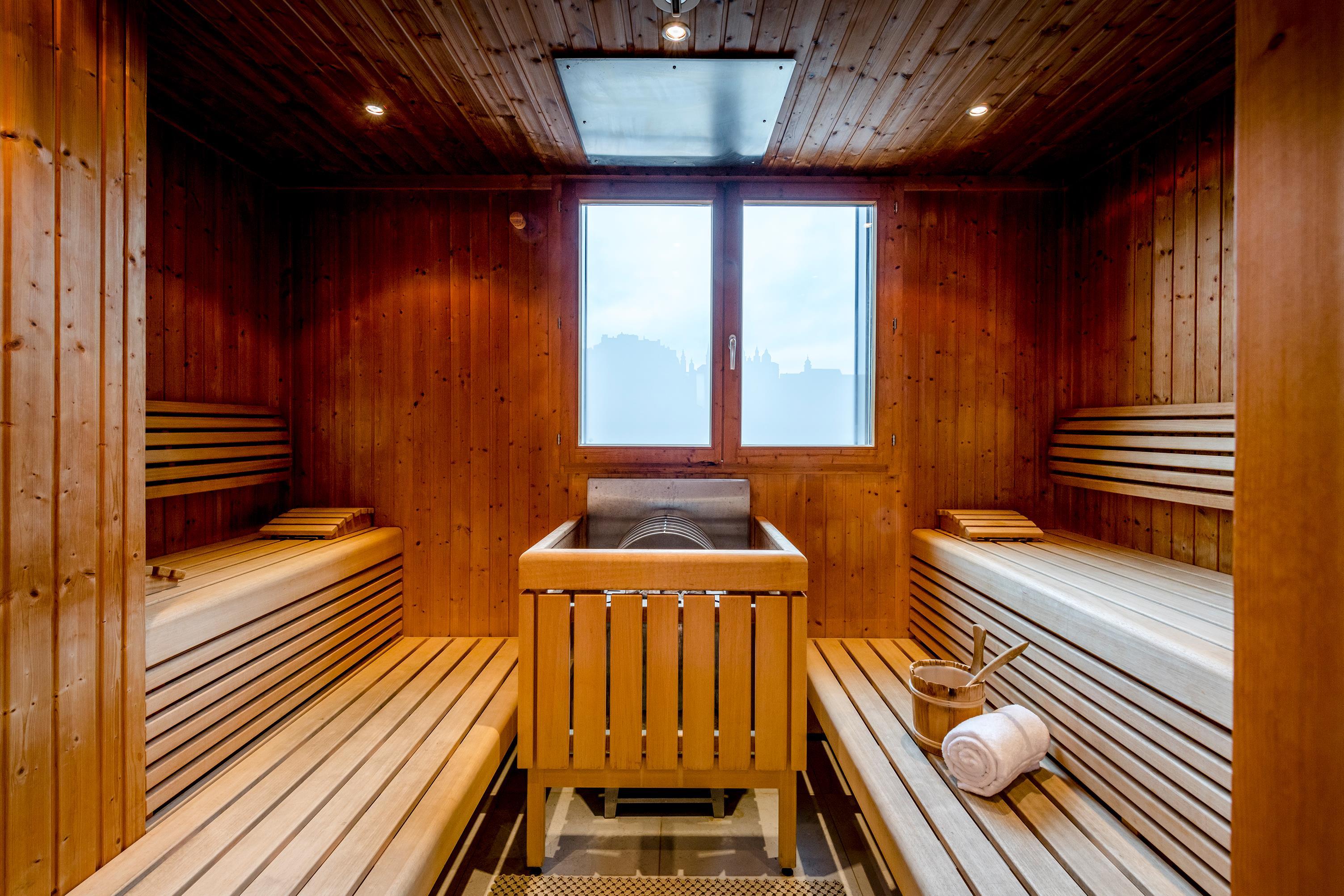 A modern sauna with wooden paneling and comfortable loungers. A large window with an outside view provides natural light.