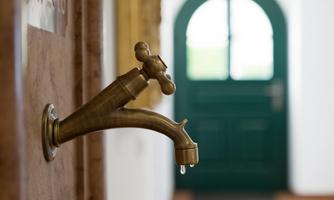 An elegant brass faucet with a droplet falling down. In the background, a green door is visible.