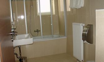 A modern bathroom with a shower and a sink. The walls are brightly tiled, and there is a towel rack as well as a hand dryer.