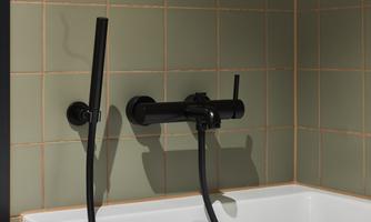 A modern bathroom with a white bathtub and black fittings. The walls are tiled in a soft green hue.