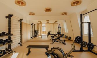 A modern gym with various training equipment. The walls are fitted with mirrors and the room is bright and inviting.