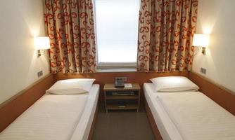 A simple room with two single beds and a modern decor. Colorful curtains hang in front of the window, and there are two wall lamps.