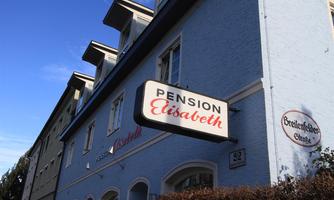 A beautiful guesthouse called "Pension Elisabeth". The facade is painted light blue and the sun is shining.