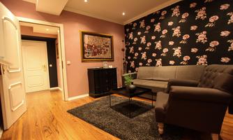 A cozy living room with a gray couch and a black coffee table. The walls are decorated with floral wallpaper in dark colors.