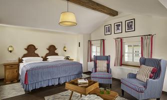 A stylish bedroom with a large bed and striped bed linen. Two comfortable armchairs and a small table complete the cozy atmosphere.