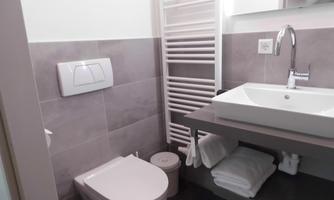 A modern bathroom with a sink, a toilet, and towels. The walls are in neutral colors, and there is a towel warmer.