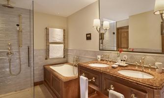 An elegant bathroom with a walk-in shower and a bathtub. The wooden vanity with two sinks and stylish lamps creates a cozy atmosphere.