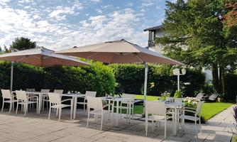 A cozy outdoor area with white tables and chairs. Umbrellas provide shade and the flowers create an inviting atmosphere.