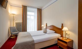 A cozy hotel room with a double bed and a bedside table. The room is bright and friendly, equipped with an armchair and a television.