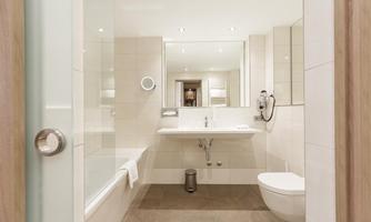 A modern bathroom with bright tiles and a large mirror. It is furnished functionally and appears fresh and clean.