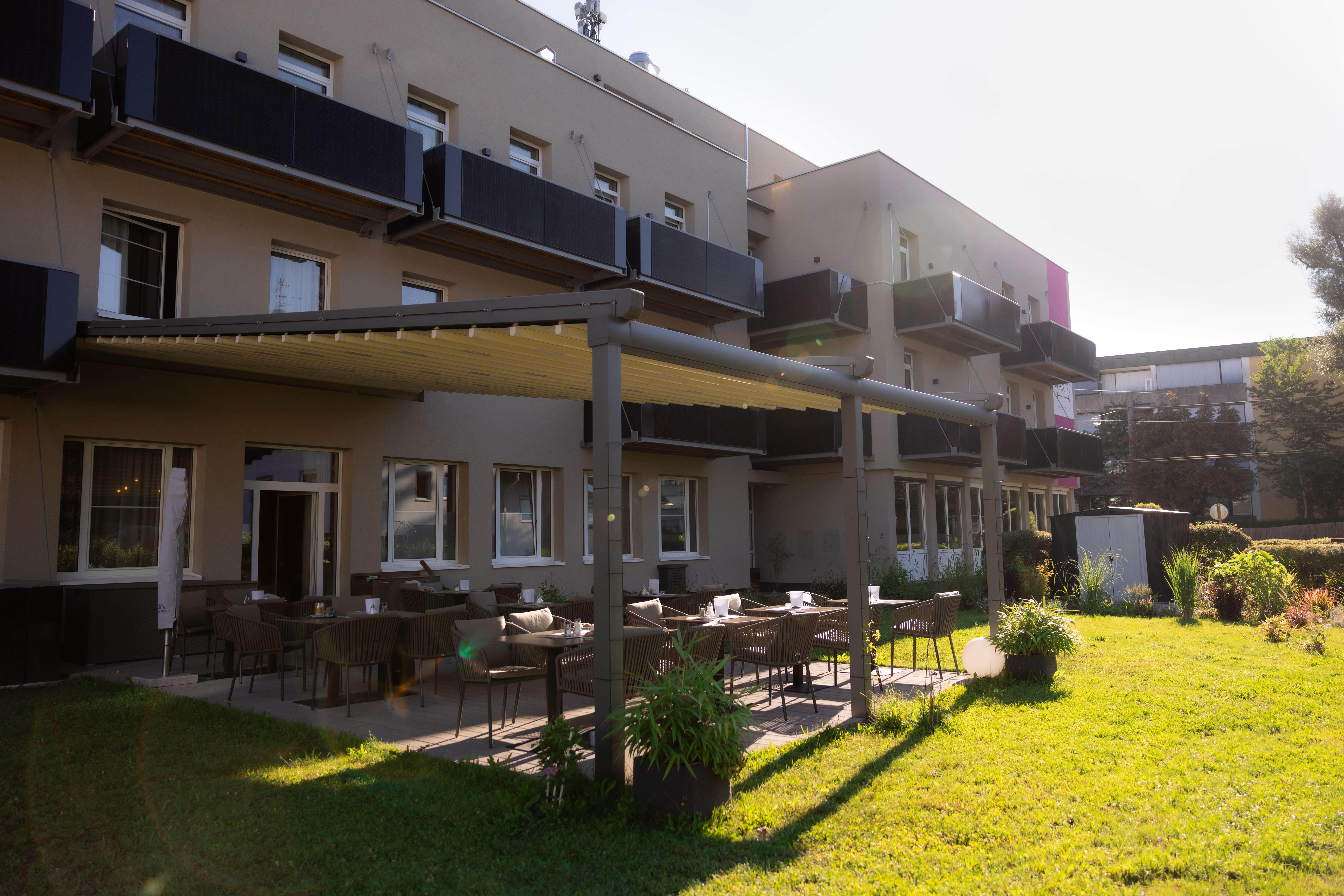 A modern building with an outdoor area and tables for seating. The garden is green and inviting, perfect for a relaxed time outdoors.