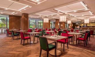 An elegant restaurant with wooden floors and stylish tables. Red and green chairs create a cozy atmosphere.