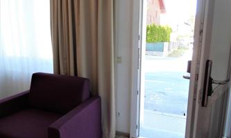 A cozy room with a purple sofa and an open entrance. Bright light streams through the window and the door.