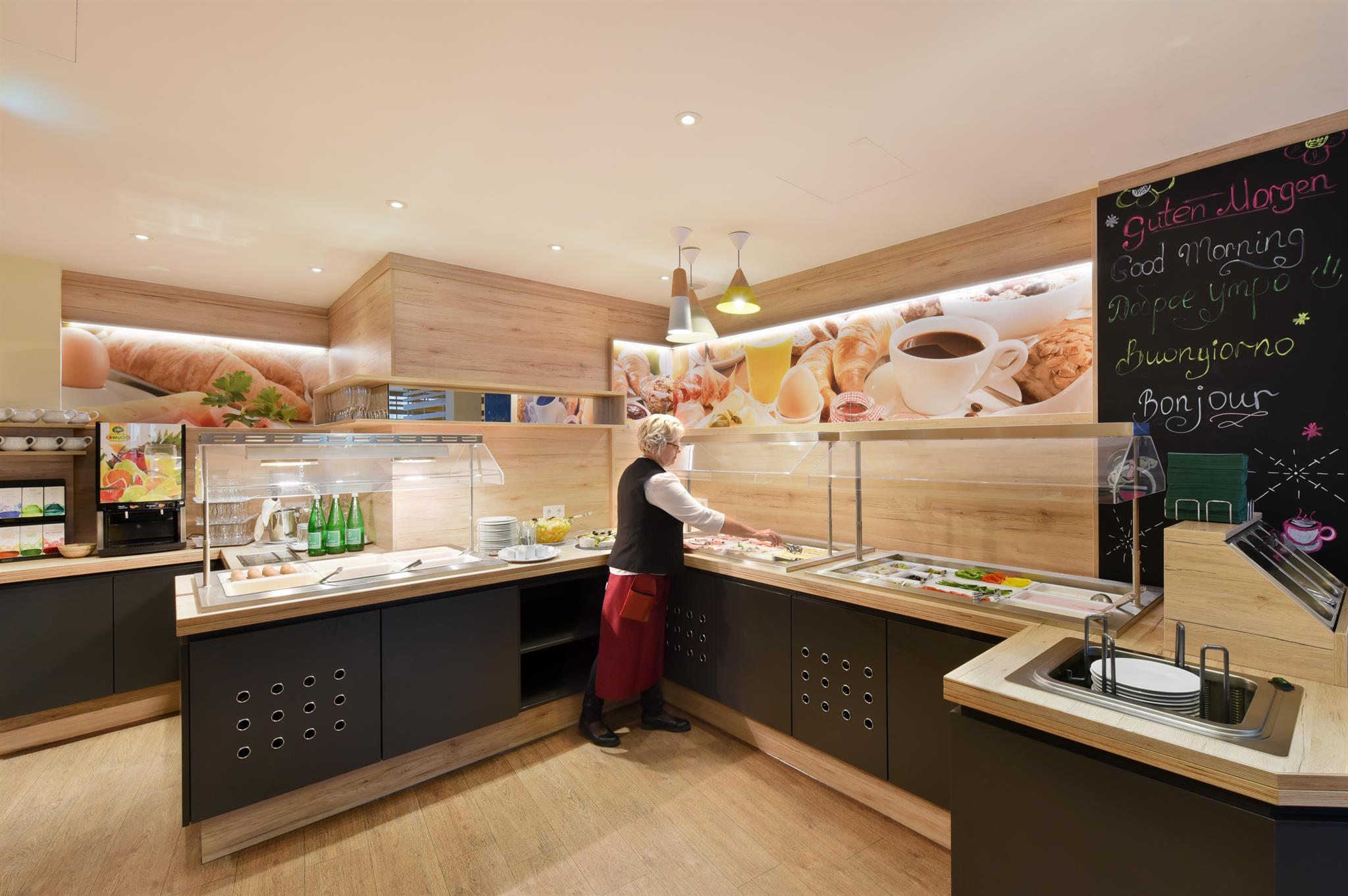 A modern breakfast area with wood decor. A person is setting up the buffet with various foods and drinks.