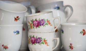 A collection of elegant porcelain cups with colorful floral designs. The cups are stacked on top of each other and are located on a shelf.