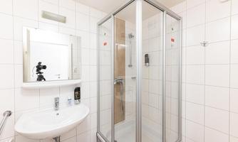 A modern bathroom with a shower and a sink. There is a large mirror and white tiles on the walls.