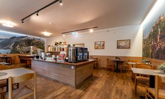 A cozy café with wooden decor and tables. In the background, there is a beautiful mural depicting a landscape.