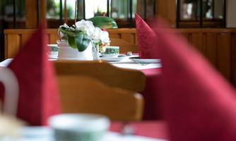 An elegant table in a restaurant, set with red napkins and fine china. In the center stands a flower that gives the room a cozy atmosphere.