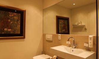 A modern bathroom with a sink, toilet, and a large mirror. The walls are painted light and there are artistic decorations.