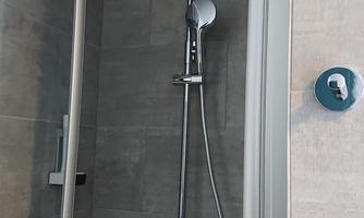A modern shower with a large rain shower head and a handheld shower. The walls are designed with gray tiles.