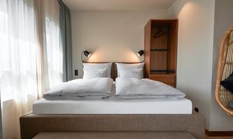 A modern hotel room with a double bed and soft colors. Large windows provide plenty of natural light and a pleasant atmosphere.