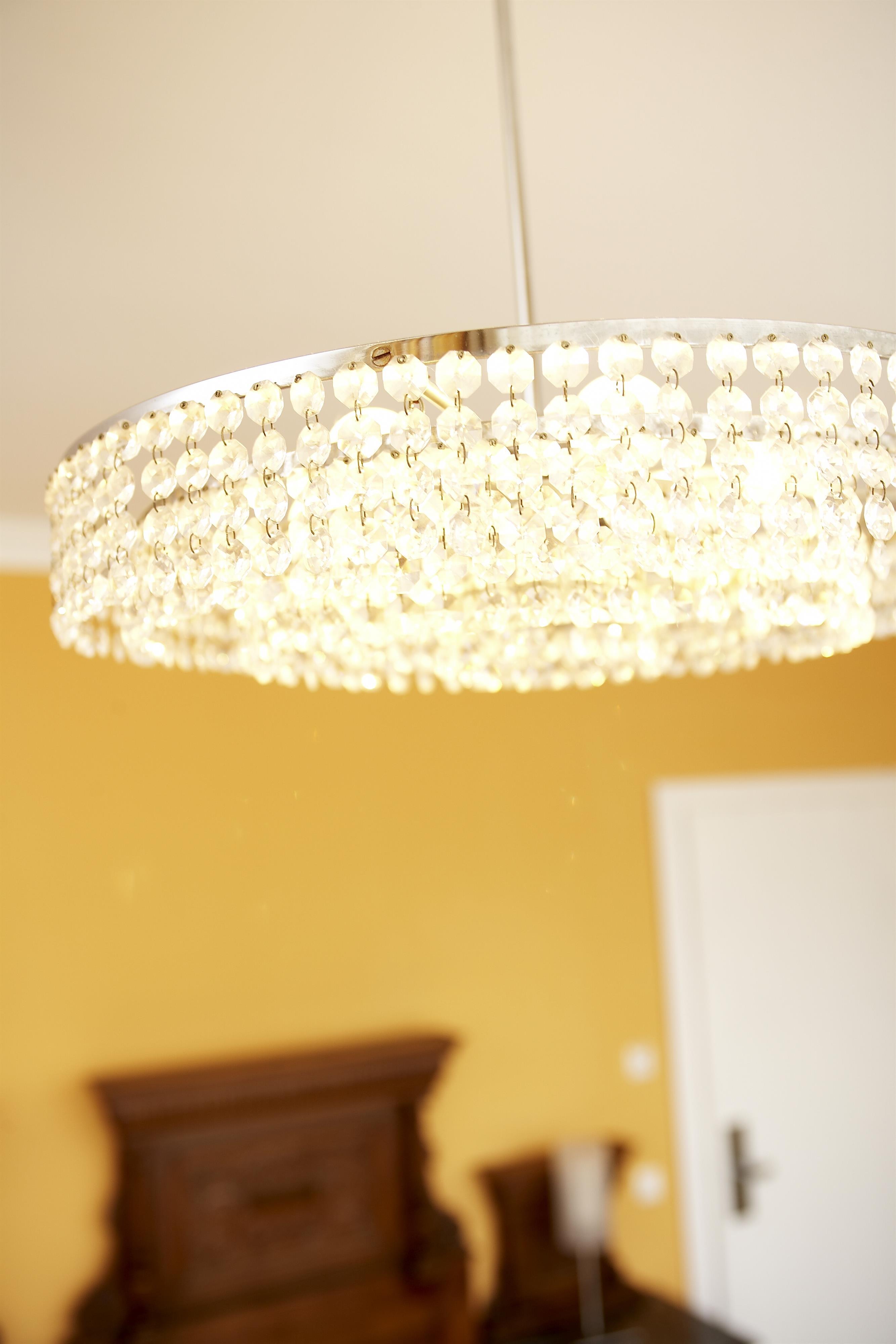An elegant ceiling light with crystals hangs in a room. The background is in warm yellow.