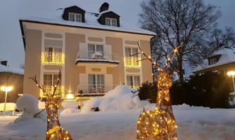 An elegant house in the snow with festive lighting. In the foreground are decorative, glowing deer.
