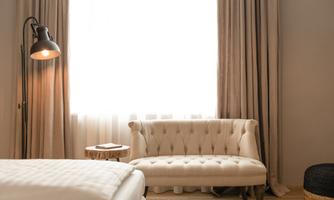 An elegant room with a bright window and a comfortable, light-colored sofa. Next to the sofa is a small side table lamp.