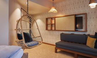 A modern living room with a hanging wicker chair and a comfortable sofa. The walls are elegantly designed and create a cozy atmosphere.