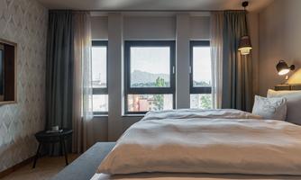 A modern hotel room with a large bed and a window that lets in plenty of light. The walls are painted in soft colors, and there is a small table next to the bed.