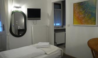 A friendly room with a cozy bed and a large mirror. A colorful painting hangs on the wall and there is a television.