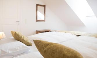 A bright bedroom with two beds and white bedding. A small mirror and a wooden dresser complement the decor.