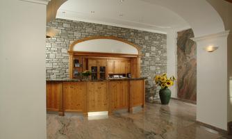 An elegant reception area with a wooden counter and a stone pattern on the wall. A large flower pot with sunflowers adds a friendly atmosphere to the room.