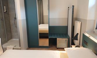 A modern hotel room with a double bed, a desk, and a bathroom area. The walls are in neutral colors, and the room feels bright and inviting.