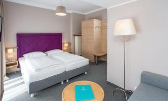 A modern hotel room with a double bed and a comfortable sofa. The walls are in neutral colors, and a round table complements the furnishings.