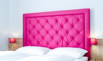 A modern bedroom with a striking pink headboard. Two nightstands with small lamps complement the bright decor.