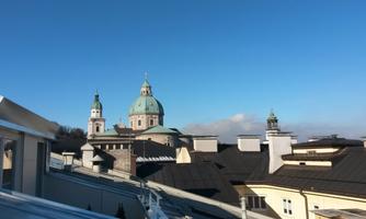 A view of a historic city with beautiful domes and a clear blue sky. The rooftops of the buildings are clearly visible.