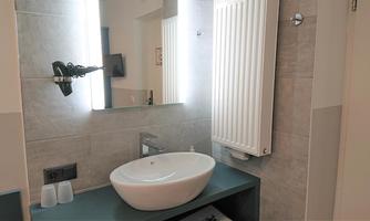 A modern bathroom with an elegant sink and a large mirror. A towel warmer is hanging on the wall and the walls are brightly tiled.