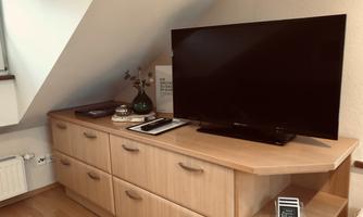 A living room with a wooden cabinet and a large television. On the cabinet are decorative items and a small plant container.