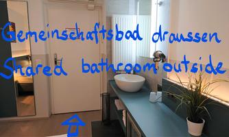 A modern bathroom with a sink and a large mirror surface. A note regarding a communal bathroom is located on the wall.