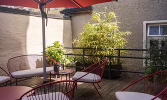A cozy terrace with red chairs and a sunshade. Plants create a green atmosphere and invite relaxation.