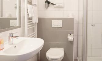 A modern bathroom with shower, toilet, and sink. The walls are tiled in white and the furnishings are functional.