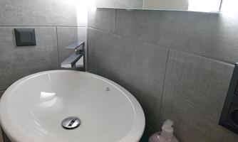 A modern sink with a round design and a faucet. The wall is clad with grey tiles.