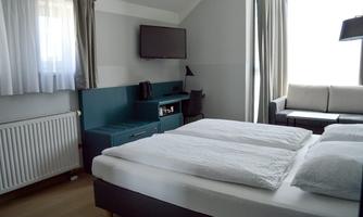 A modern hotel room with a large double bed and a cozy sofa. The room is bright and friendly with a TV and a desk.