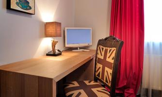 A simple workspace with a wooden desk, a chair in Union Jack design, and a monitor. Red curtains add a colorful accent to the room.