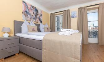 A modern bedroom with a large bed and cozy bedding. The walls are painted in a warm shade of yellow, and large windows let in plenty of light.