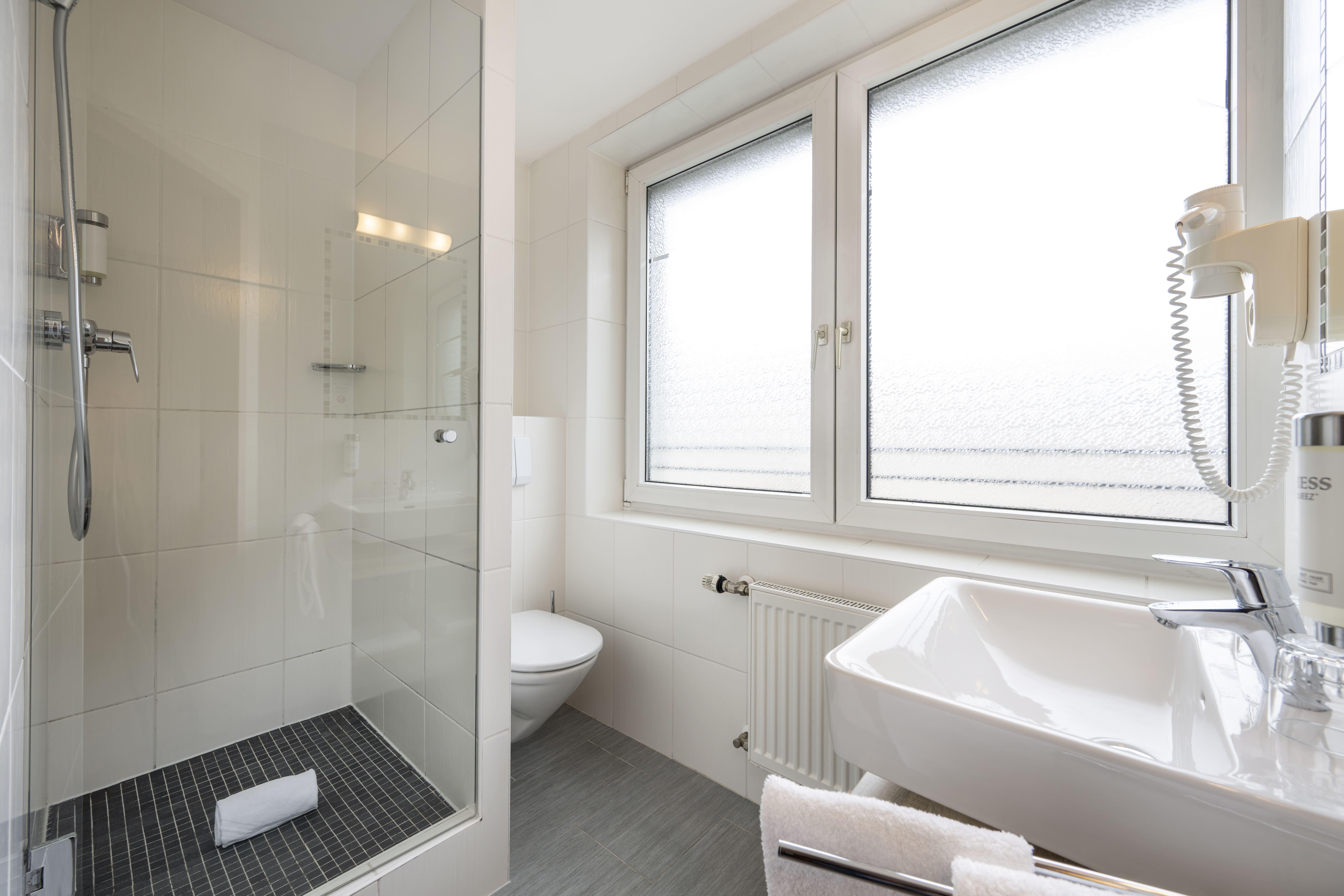 A modern bathroom with a shower and a sink. The window provides daylight and a bright atmosphere.