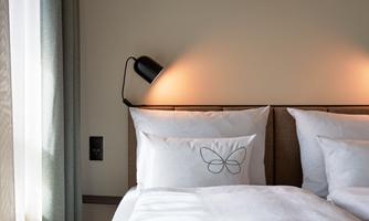 A cozy bedroom with a double bed and elegant pillows. Soft lighting and curtains create a relaxing atmosphere.