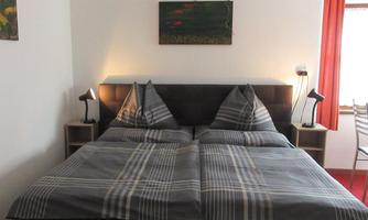 A cozy bedroom with a double bed and modern nightstands. The walls are painted light, and there are decorative pictures as well as warm light from the lamps.